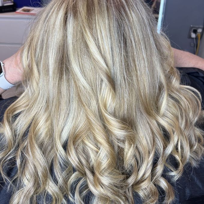 Long blonde balayage seen from behind, brushed into loose waves with pale ribbons running through the mid-lengths and ends.
